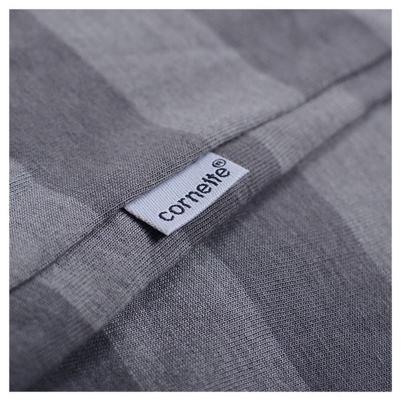 Metka marki Cornette na szarej tkaninie – detal bluzy z paskami.