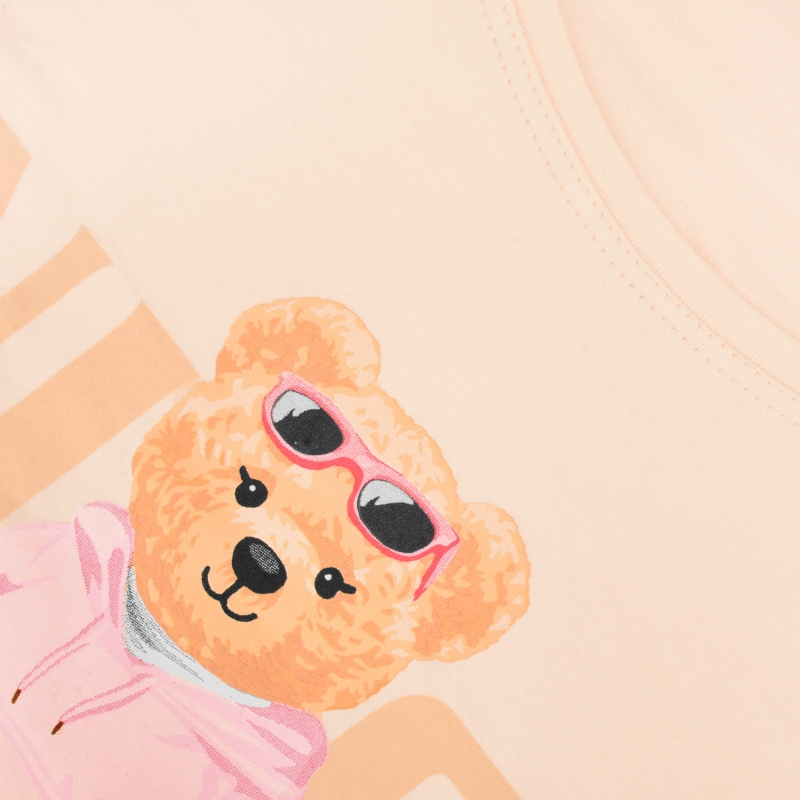 Zbliżenie na beżową koszulkę piżamową z nadrukiem misia w różowych okularach i bluzie.