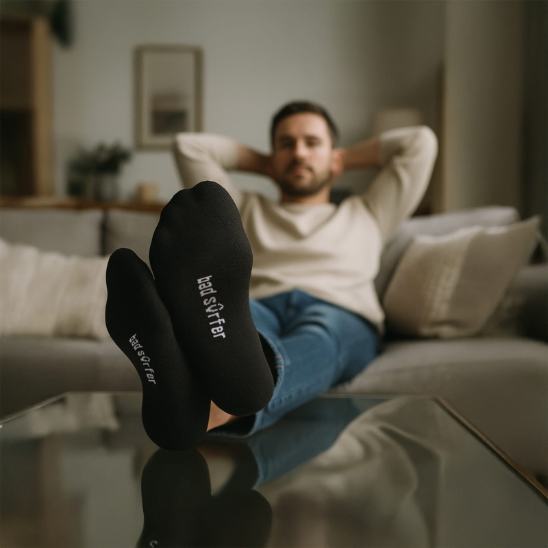 Mężczyzna w stopek Bad Surfer siedzi na kanapie, widoczne logo na spodzie stóp