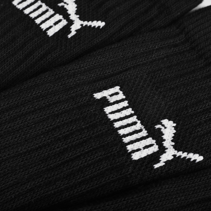 Zbliżenie na materiał i biały nadruk Puma na czarnych skarpetkach.